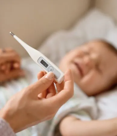 Mão segurando termômetro perto de bebê feliz.