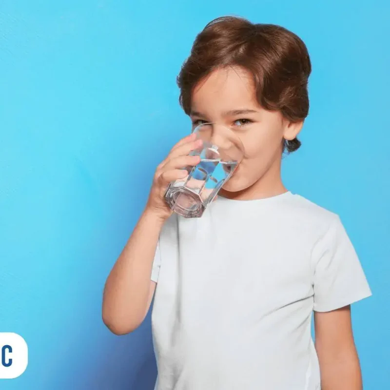 Criança de camiseta branca bebendo água, ao fundo parede no tom azul claro