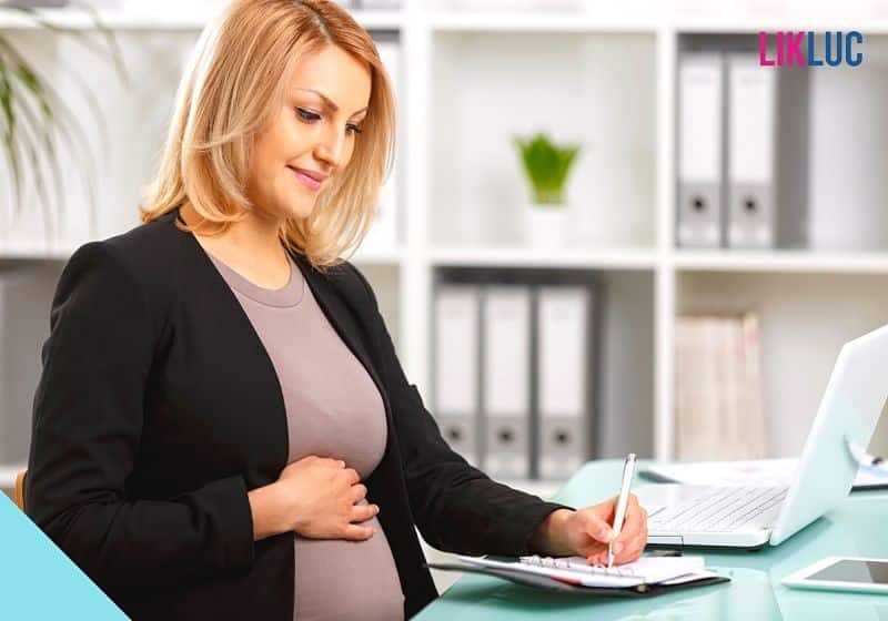Mulher grávida com a mão na barriga e trabalhando