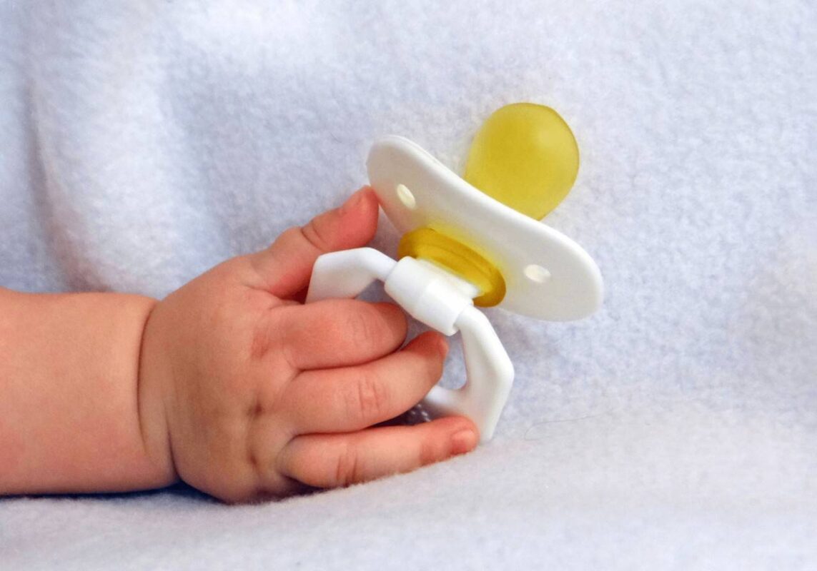 Detalhe de mão de bebê segurando chupeta amarela