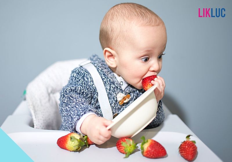 Bebê comendo morangos em cadeirinha de alimentação