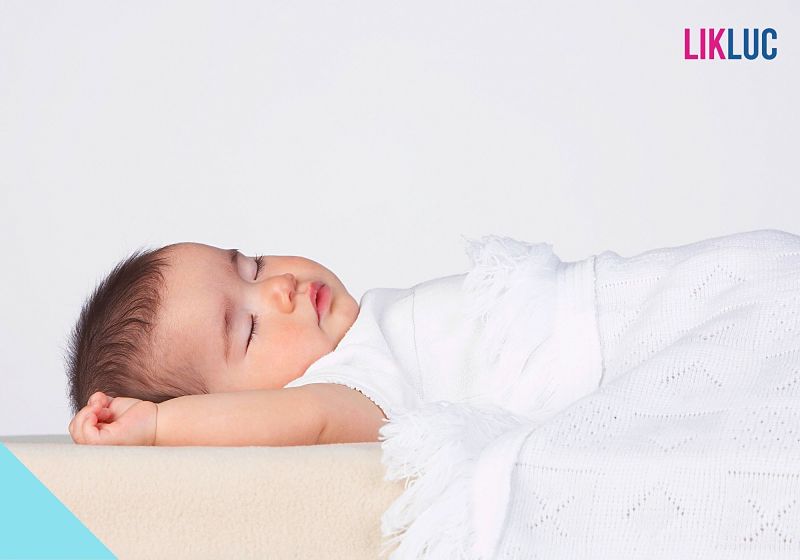 Bebê dormindo tranquilamente envolto em um cobertor branco.