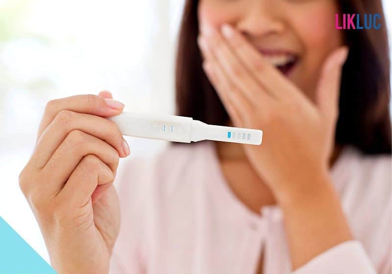 mulher segurando teste de gravidez com mão na boca sorrindo