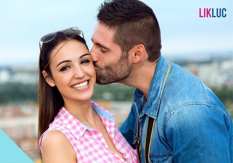 moça sorrindo olhando para frente enquanto moço beija sua bochecha
