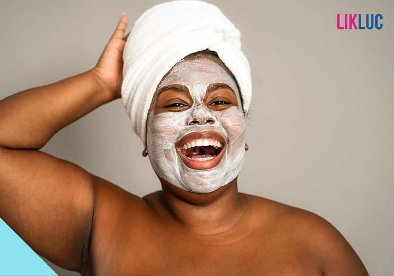 mulher sorrindo com máscara facial branca e segurando a toalha enrolada na cabeça