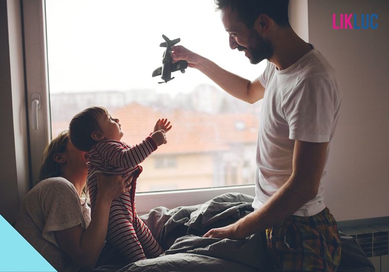 Pai brincando com filho e mãe ao fundo