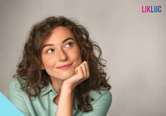 Mulher de cabelo ondulado, rosto apoiado na mão e com um olhar inclinado para a esquerda