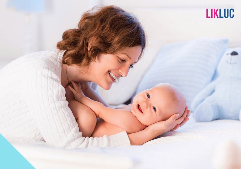 como identificar os dentes rasgando a gengiva mae segurando bebe deitado na cama e os dois sorrindo