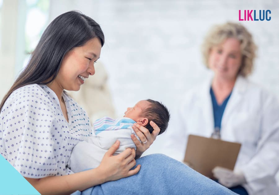 mae sentada na maca de maternidade segurando bebe virada para si sorrindo e medica atras