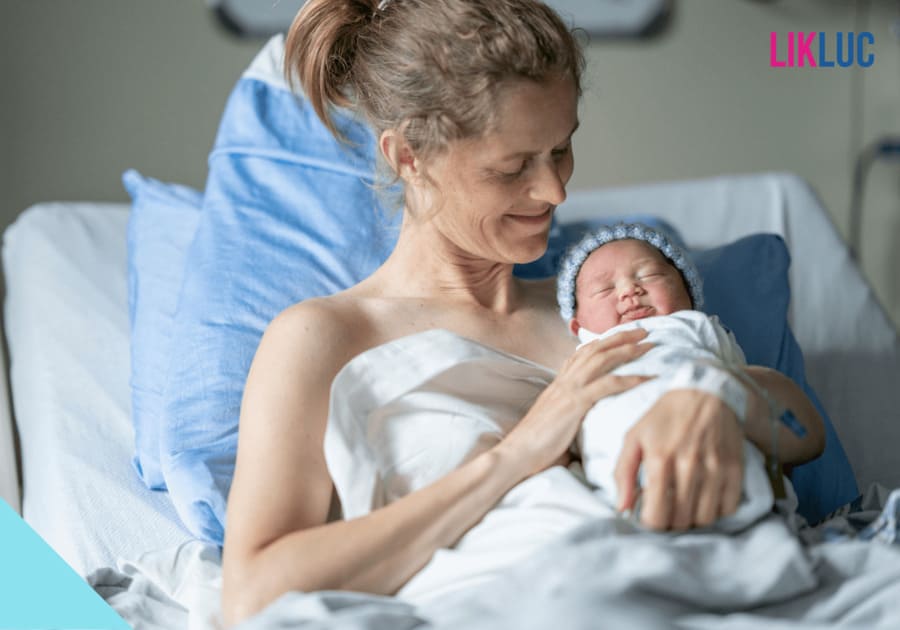 mae segurando bebe enrolado em lencol na cama do hospital e sorrindo