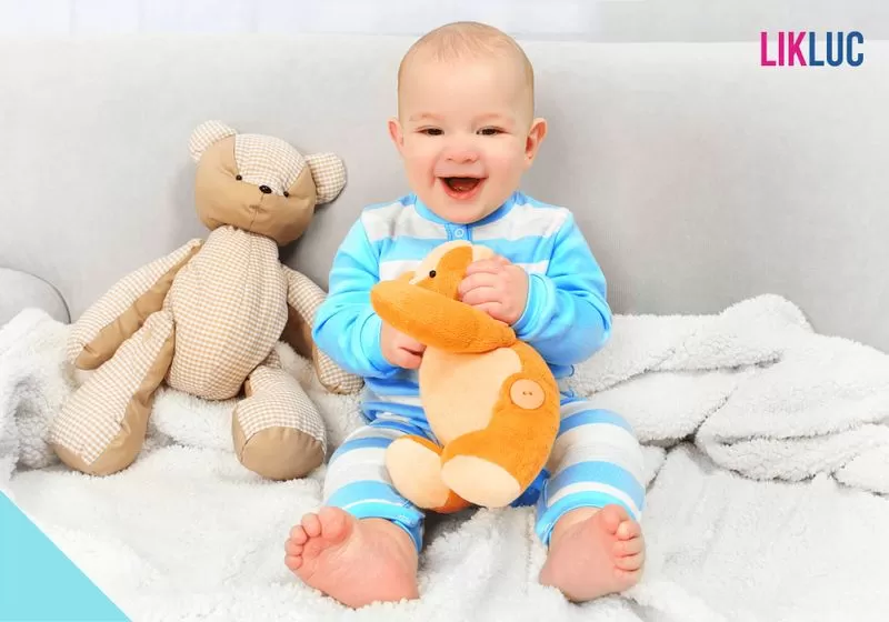 bebe sentado segurando sua naninha e sorrindo para foto