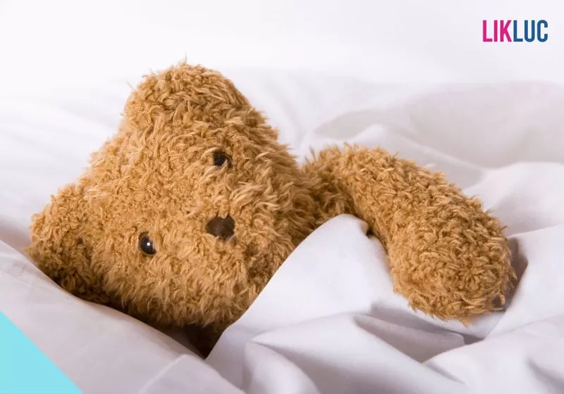 ursinho de pelucia se cobrindo e deitado em cama