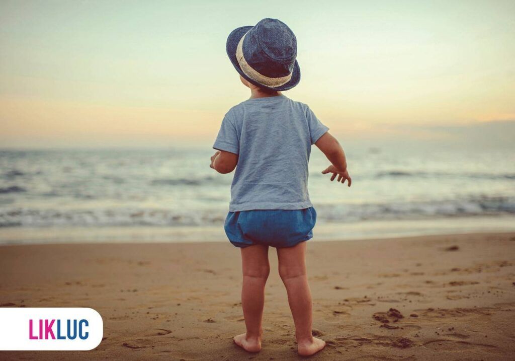 Bebê usando roupinha e chapéu na praia