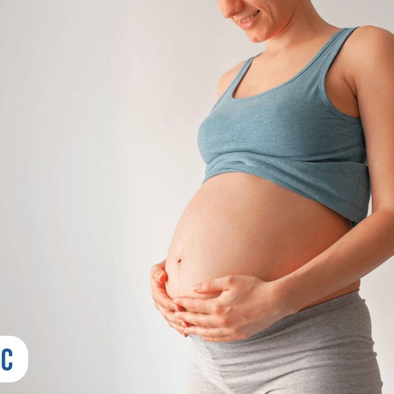 Gestante sorrindo com suas mãos na barriga