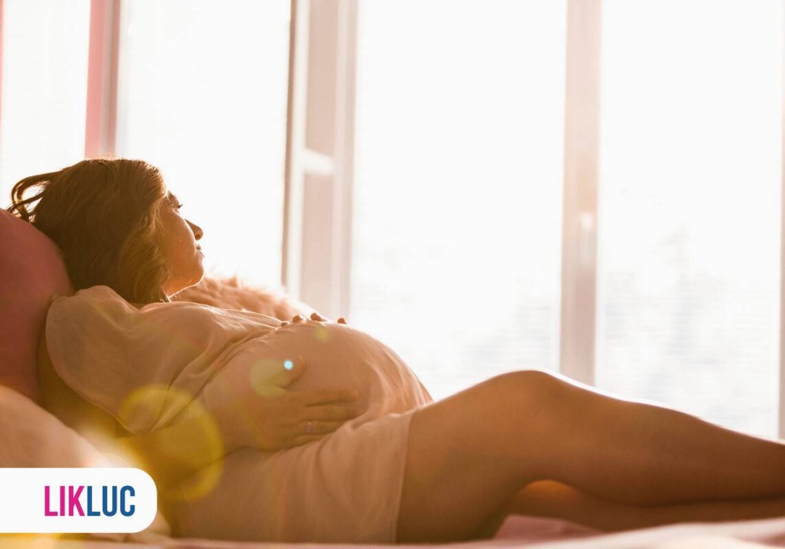 Gestante olhando pela janela e segurando a barriga