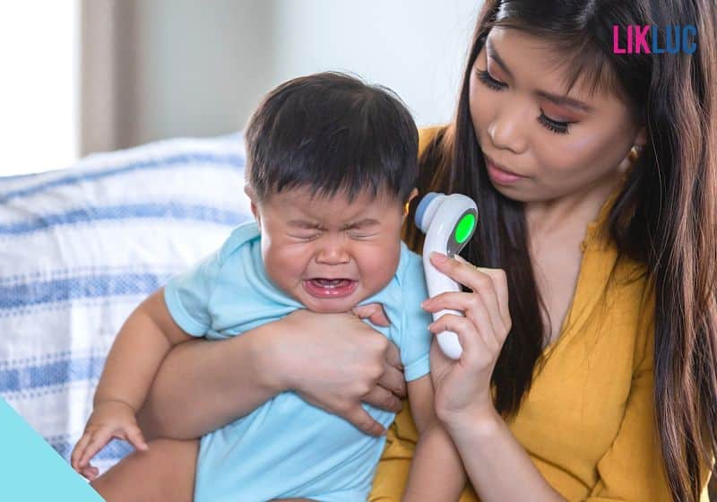 Bebê chorando no colo da mãe enquanto a temperatura é medida