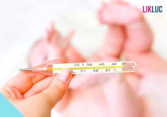 Mãe com um termômetro de vidro e o bebê ao fundo deitado
