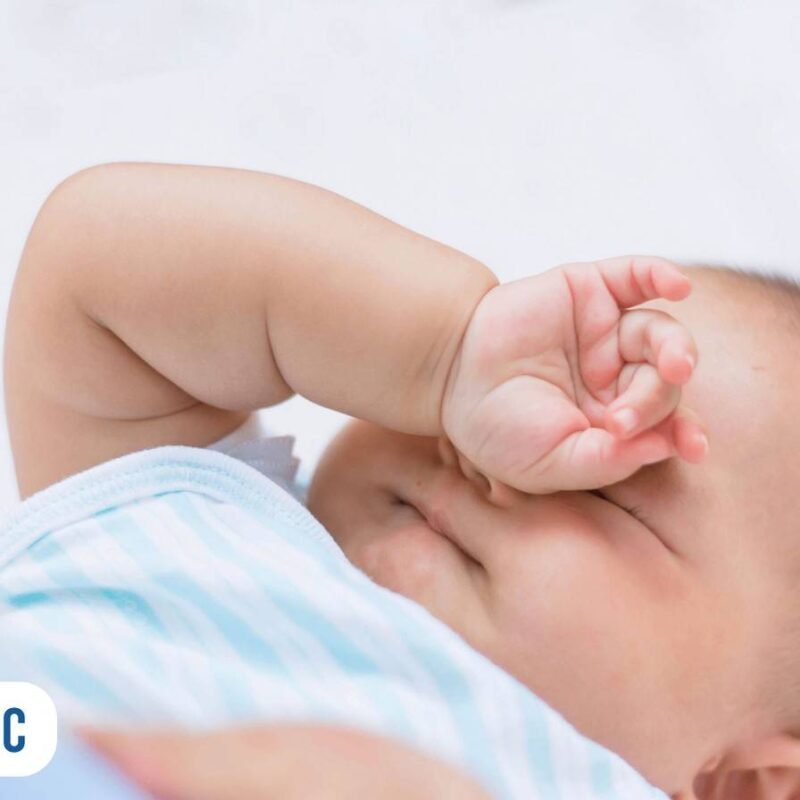 bebe deitado coçando o próprio olho com a mãozinha