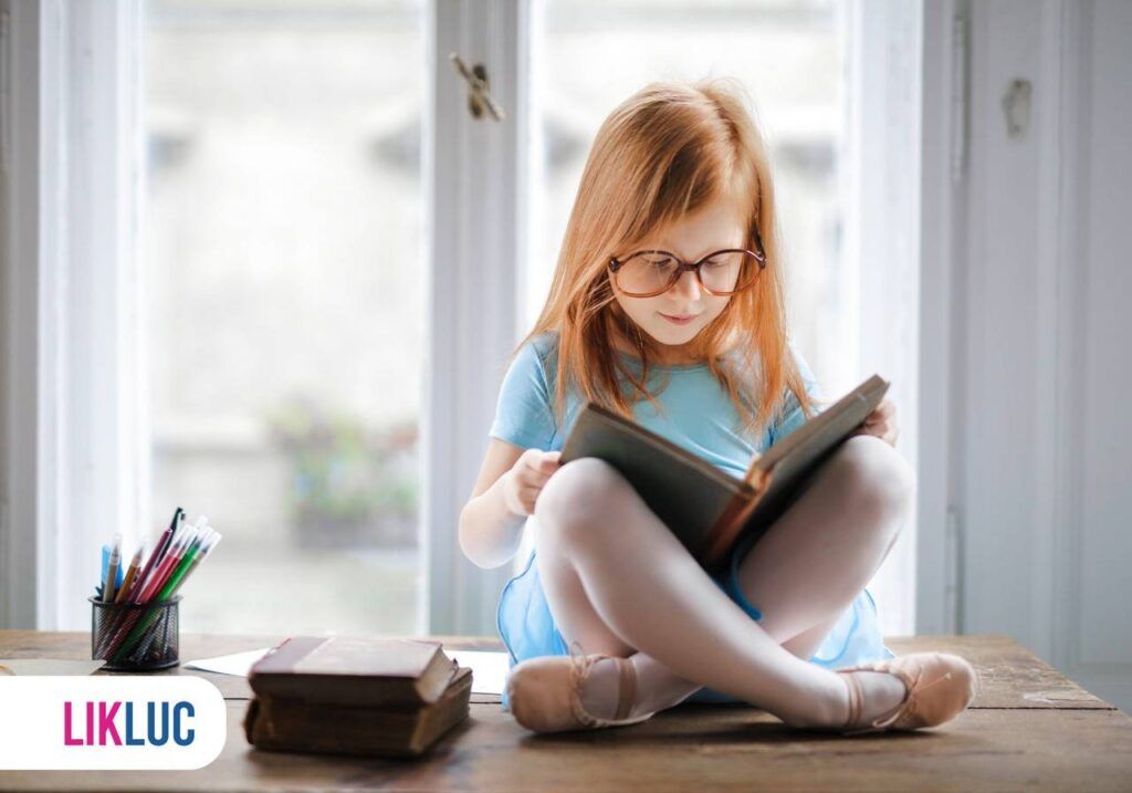 criança sentada lendo livro apoiado nos joelhos e usando óculos