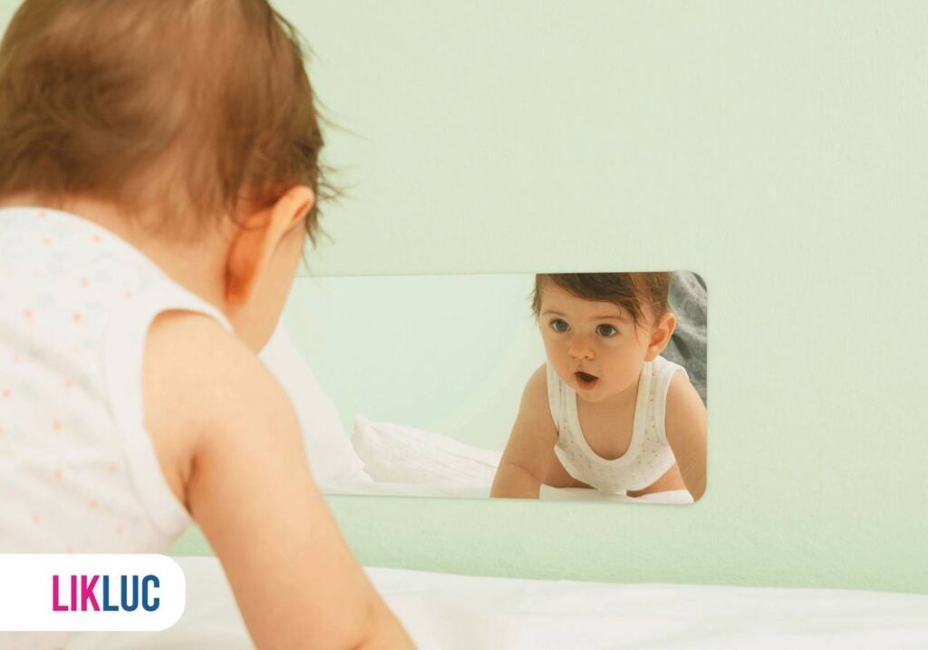 Bebê na posição de engatinhar, usando roupas brancas, olhando própria imagem refletida no espelho