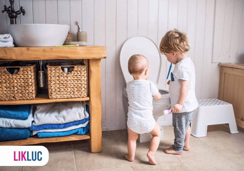 Criança e bebê posicionados ao lado de vaso sanitário