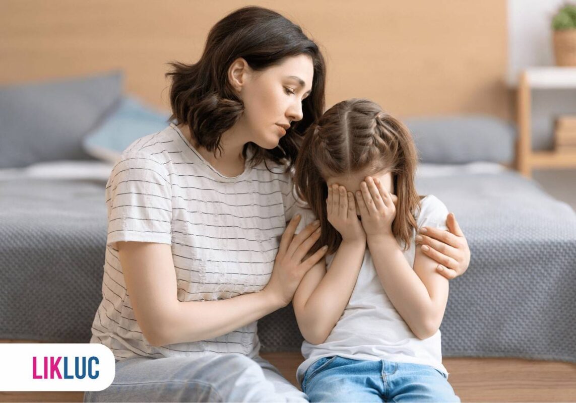 Criança com as mãos no rosto chorando, ao lado, sua mãe abrançcando e consolando