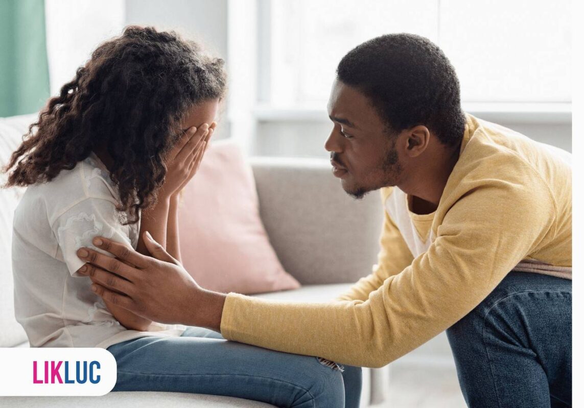 Criança sentada no sofá com as mãos no rosto e chorando, seu pai agachado e a consolando