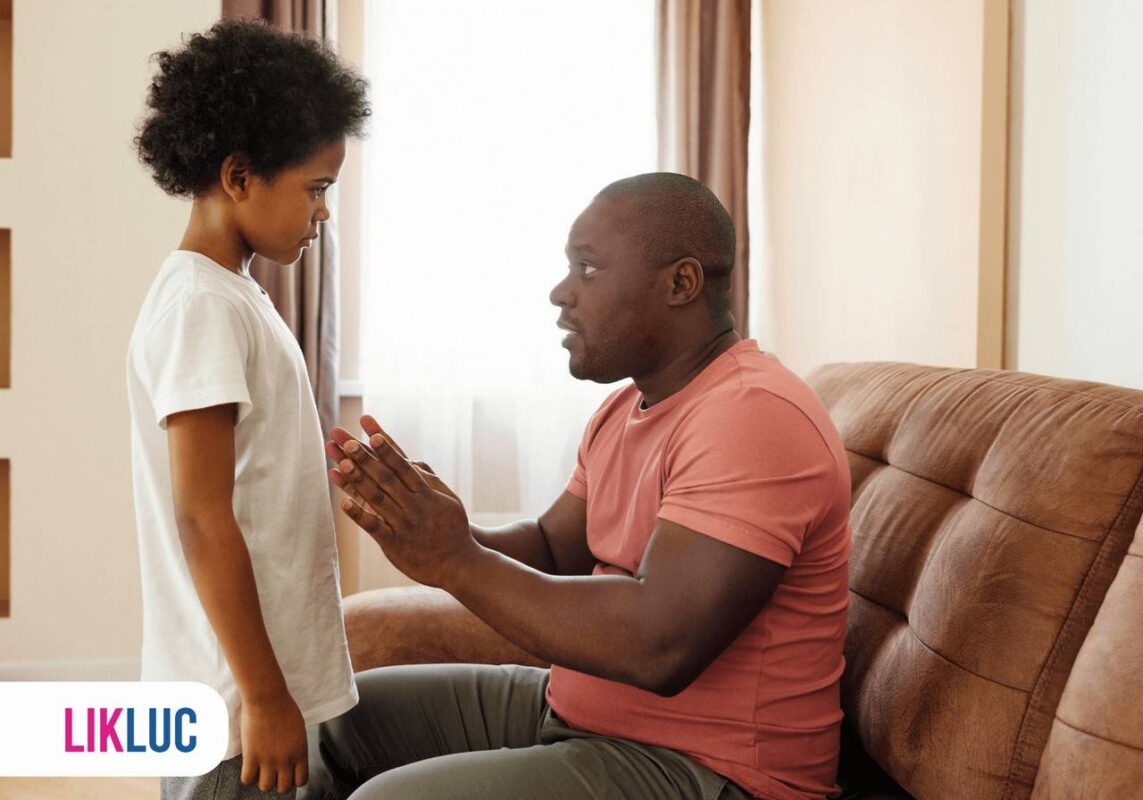 Pai sentado em sofá da sala orientando filha que está a sua frente e de pé