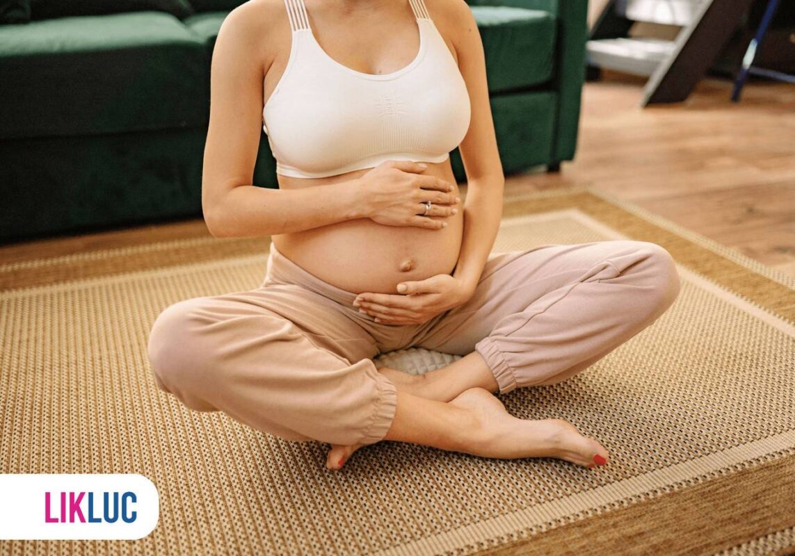 Gestante sentada ao chão com as duas mãos na barriga