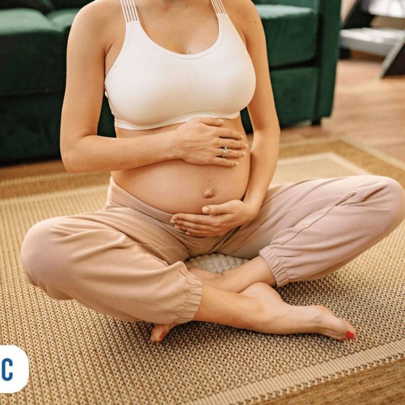 Gestante sentada ao chão com as duas mãos na barriga