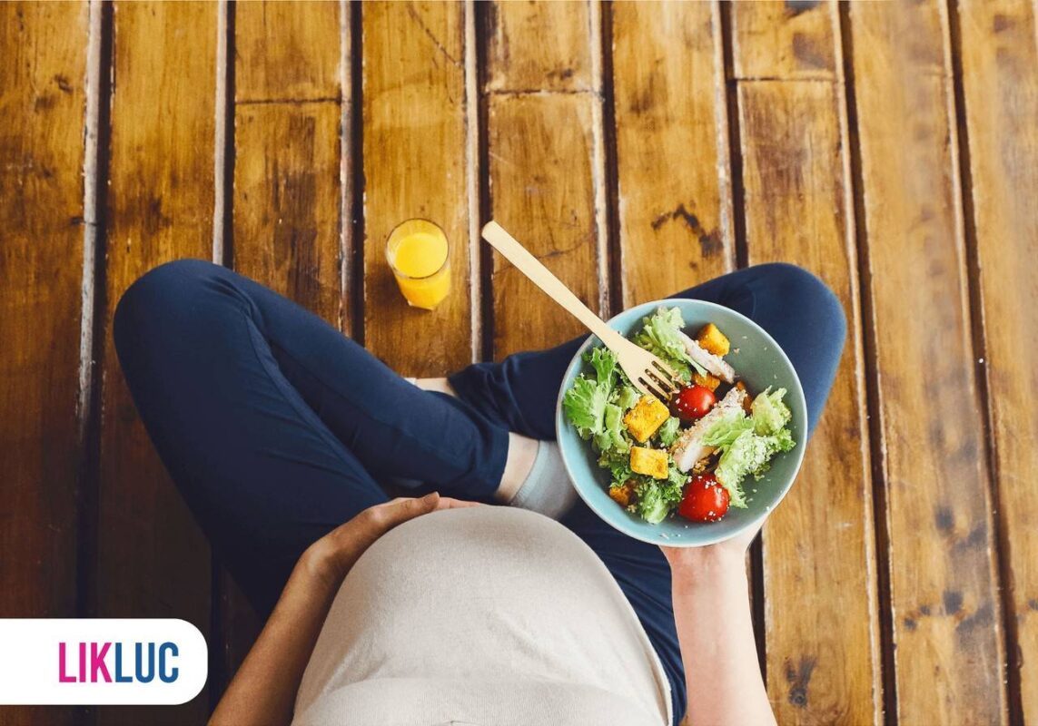 Gestante com mão na barriga e segurando uma prato com salada e grãos