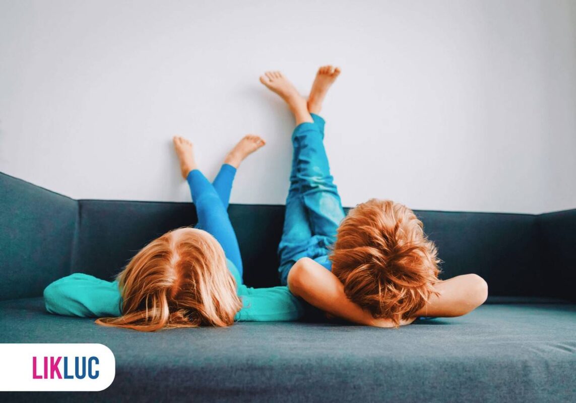 Duas crianças deitadas no sofá de ponta cabeça e com pés nas paredes