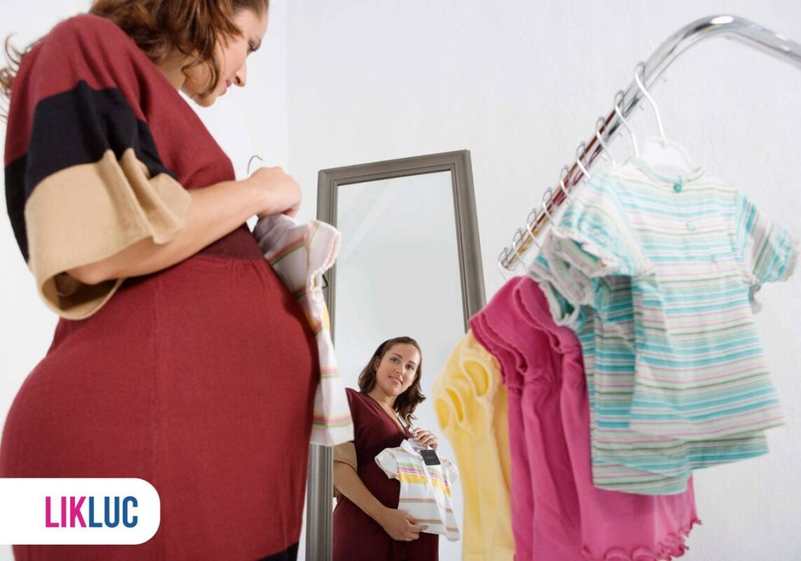 Grávida com vestido vermelho colocando roupa de bebê na barriga