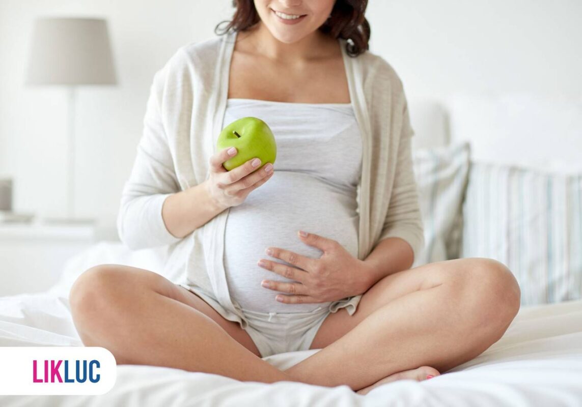 Mulher grávida segurando uma maçã com a mão na barriga
