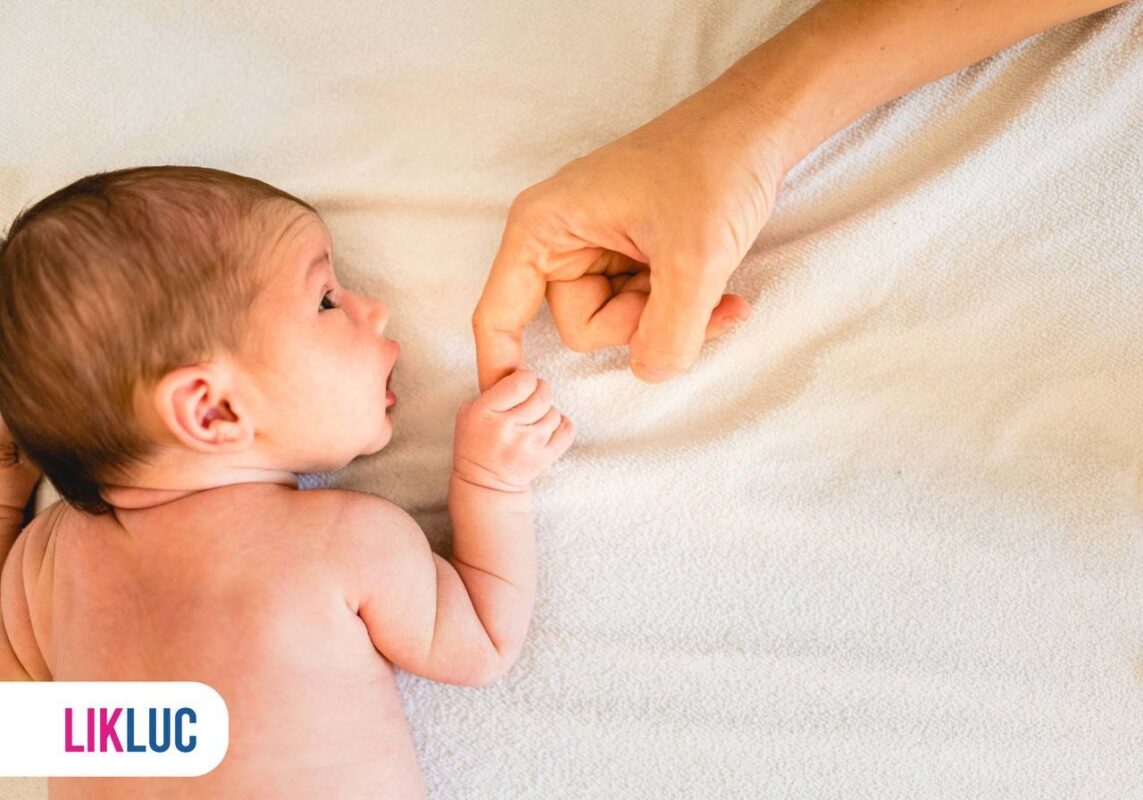 bebê recém nascido deitado de barriga pra baixo segurando o dedo da mão de uma pessoa