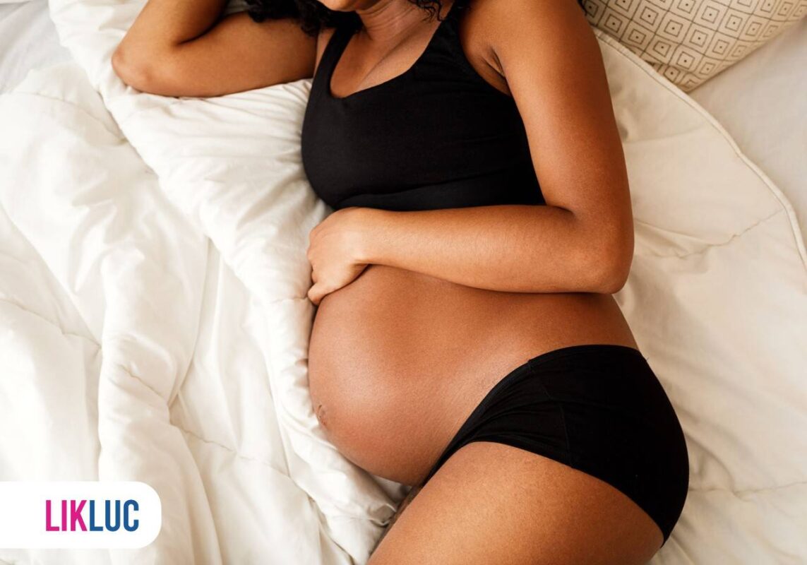 Mãe grávida com mão na barriga e deitada na cama