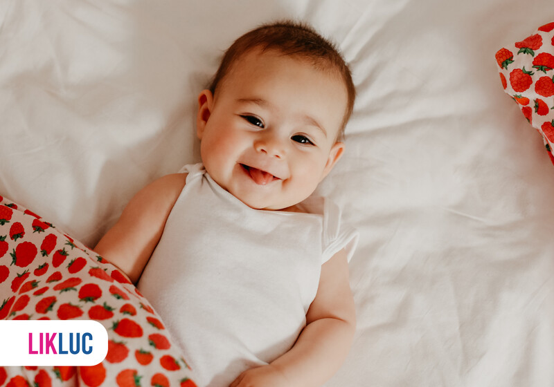 Bebê sorrindo em cama com lençol de morangos.