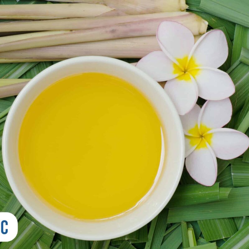 Óleo aromático de citronela ao lado de flores e folhas verdes