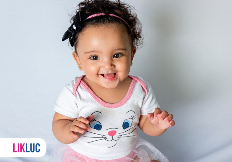 Bebê sorrindo com camiseta de coelho e laço preto.