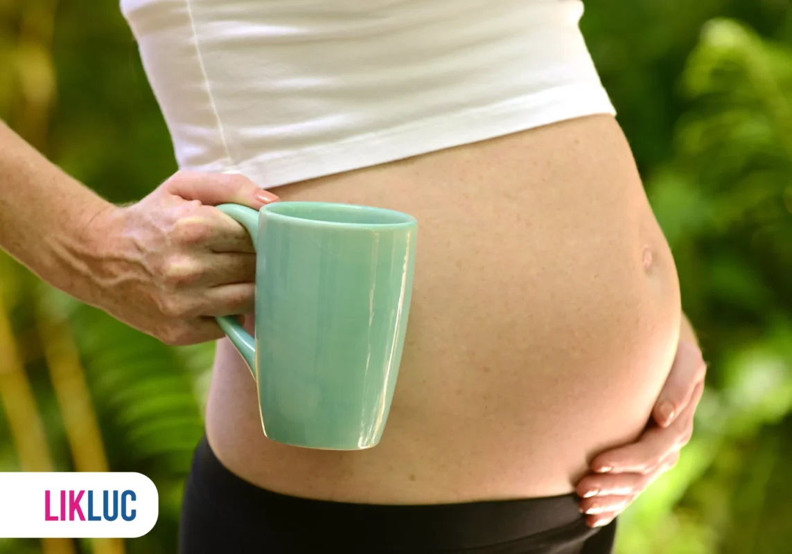 Mão segurando caneca sobre barriga de grávida