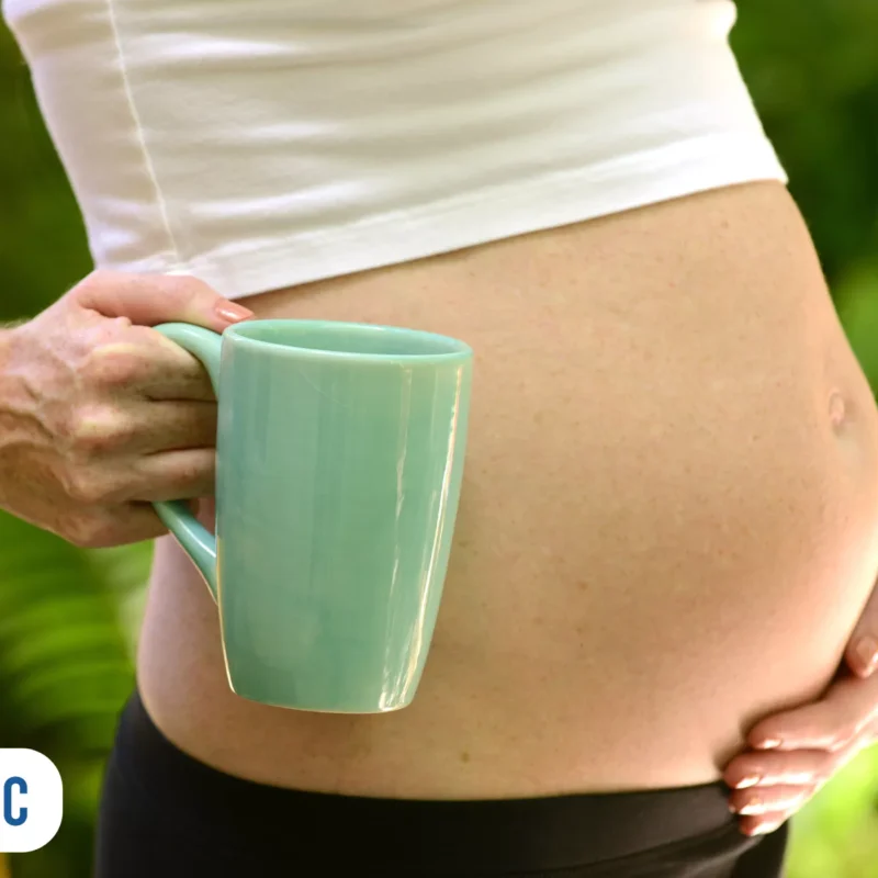 Mão segurando caneca sobre barriga de grávida
