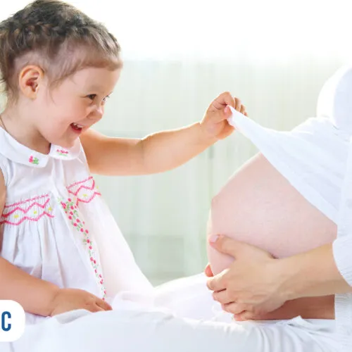 Criança sorrindo e tocando barriga de grávida