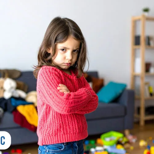 Criança com expressão séria em sala bagunçada
