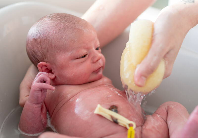 Bebê tomando banho em uma bacia, sendo limpo com sabão