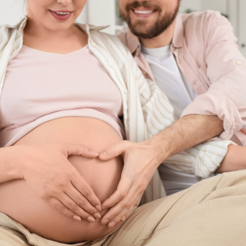 Casal sorridente fazendo coração na barriga de grávida.
