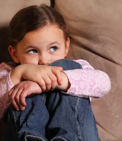 Criança encolhida em sofá, olhando para o lado.