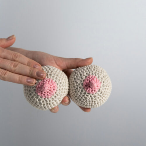 Mãos segurando peças de crochê em formato de seios.