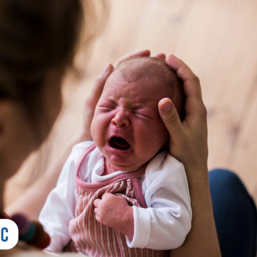 Bebê chorando nos braços da mãe em ambiente aconchegante