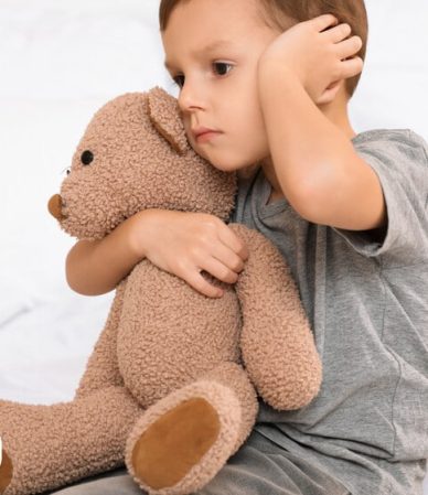 Criança abraçando urso de pelúcia e parecendo triste.