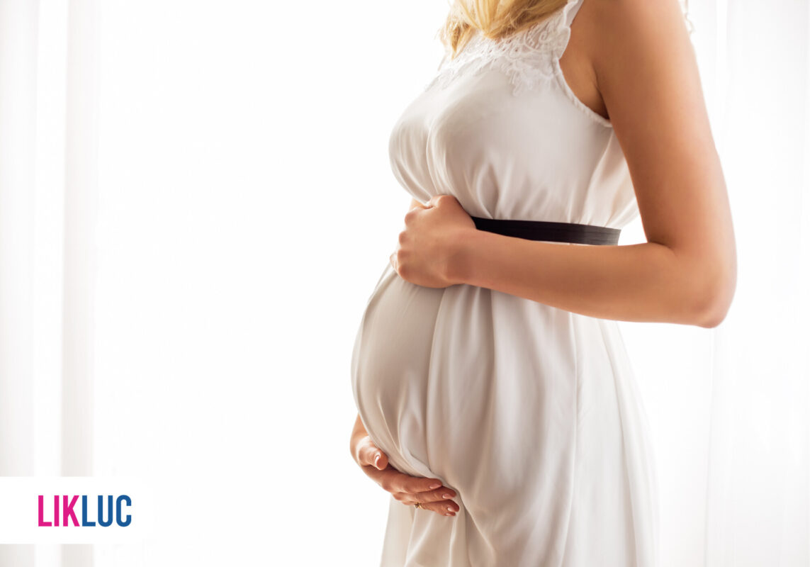 Mulher grávida em vestido claro segurando a barriga